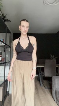 Top halter preto com acabamento em renda, combinado com calças largas bege pregueadas; apresenta padrões subtis e uma textura suave.