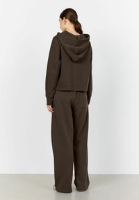 Felpa corta marrone con cappuccio e tasca a marsupio, abbinata a pantaloni a gamba larga con tasca posteriore, entrambi in un tessuto morbido.