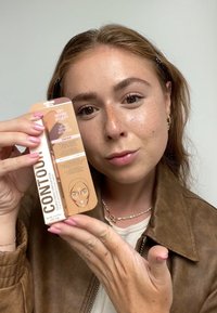 Confezione di bastoncini per il contouring in una combinazione di colori oro e pesca, con un'illustrazione del viso e dettagli del prodotto sul retro.