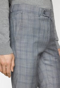 Pantaloni a quadri grigi realizzati in tessuto liscio, con davanti piatto, tasche laterali e una vita con bottone singolo.
