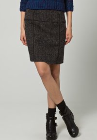 Falda lápiz de tweed gris con tejido texturizado, hasta la rodilla, con detalles sutiles de costuras y una cinturilla discreta, combinada con botines negros hasta el tobillo.