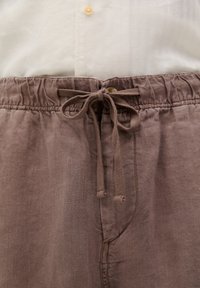 Linnedragt i en lys brun farve med elastisk talje og frontknude. Har en sidelomme og en blød, struktureret finish.