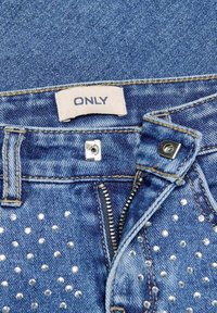 Modre jeans hlače iz denima z zadrgo spredaj, srebrnim gumbom in okraski iz majhnih prozornih kroglic na eni strani. Znamka je označena kot "ONLY."