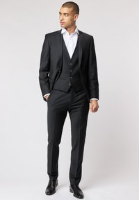 Schwarzer dreiteiliger Anzug mit slim Fit, spitzem Revers und einem weißen Hemd. Kombiniert mit schwarzen eleganten Schuhen, glattem Stoff und maßgeschneidertem Design.