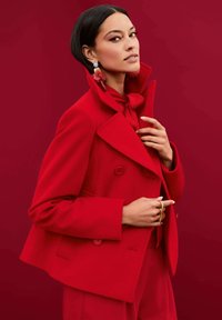 Roter Wollmix-Peacoat mit doppelt knöpfbaren Knöpfen, breiten Revers und verkürztem Schnitt. Zubehör umfasst große Ohrringe mit Drop-Design.