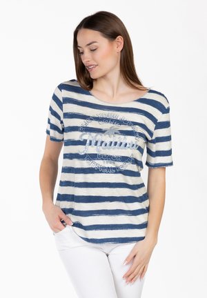 Donna che indossa pantaloni bianchi e una maglietta a righe blu e bianche con la scritta "Hawaii Beach Tropical Escape" e un disegno di palma.