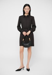 Melnas pogājamas kleitas ar garām piedurknēm un savilktu jostasvietu; apvienota ar mazu, izliekta melna rokas somu un melniem kurpēm ar asu purngalu.