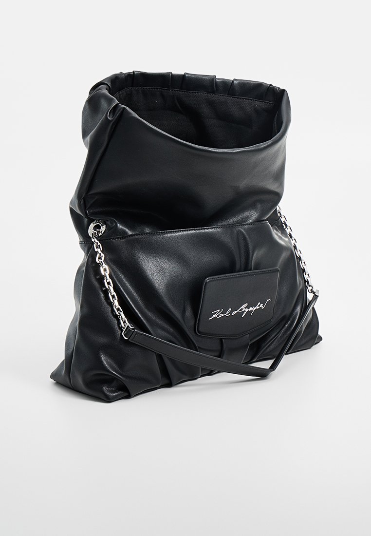Sac slouchy en simili cuir noir avec chaîne et bande. Il possède une poche avant avec un logo en relief. Texture lisse, haut arrondi.