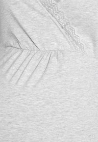 Ανοιχτό γκρι τοπ με υφή, διακοσμημένο με δαντέλα κατά μήκος του λαιμού και με πιέτες στη μέση για επιπλέον σχήμα.