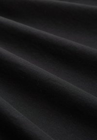 Zwart katoenstof met een gladde textuur, met subtiele plooien en vouwen, die de flexibiliteit en het gewicht van het materiaal accentueren.