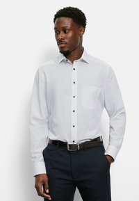 Witte lange mouwen overhemd met knopen, voorzien van marineblauwe stippen, een klassieke kraag en blauwe knopen, gecombineerd met donkere broek en een bruine riem.