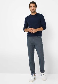 Marineblauwe gebreide trui gecombineerd met gestructureerde grijze broeken. Model draagt witte sneakers met blauwe accenten. Eenvoudige, casual outfit weergegeven.