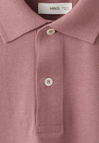 Polo mauve clair avec col court et deux boutons blancs, montrant l'étiquette de la marque MNG à l'intérieur du col.