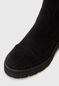 Bottine en daim noir avec un bout arrondi, surface texturée et semelle en caoutchouc robuste contrastante présentant des détails de couture le long des bords.