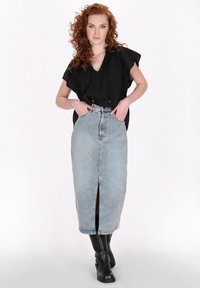 Sort kortærmet top med v-hals, parret med en lys blå denim midi-nederdel med en frontal slids. Modellen bærer sorte knæhøje støvler.