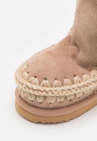 Bottine en suède beige avec des coutures en jute tressé autour de l'orteil et une semelle texturée. Présente une forme arrondie et un matériau doux.