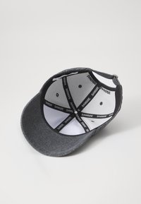 Grå baseballcap med buet skjerm, teksturert stoff og en svart og hvit innside med merkede sømmer og ventilasjonsluker.