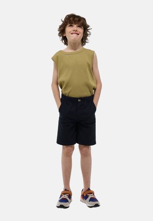 Un haut sans manches vert olive et un short noir avec une taille élastique. Le garçon porte des baskets multicolores avec des semelles blanches.