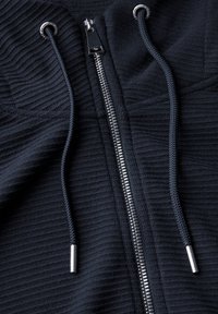 Sudadera con cremallera negra, con textura acanalada, cremallera plateada y cordones a juego con puntas de metal.