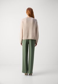 Pull en tricot beige à coupe décontractée, associé à un pantalon vert taille haute. Le pantalon est ajusté avec une texture lisse et une coupe droite.