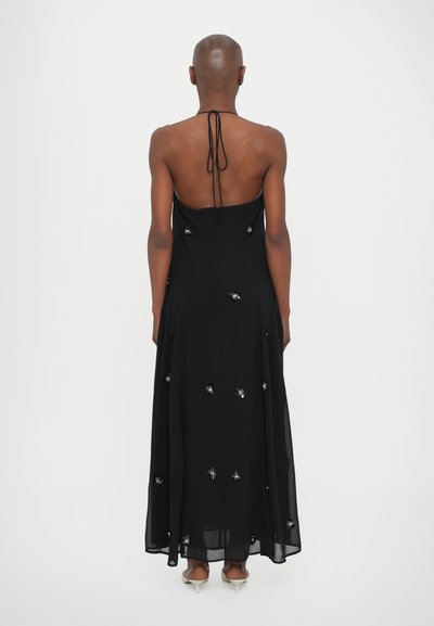 Black halter maxi dress featuring a low back, side slits, and silver floral embellishments throughout. Lightweight fabric with a flowing design.