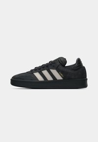 Μαύρο αθλητικό παπούτσι Adidas Samba με λευκές ρίγες, επάνω μέρος από σουέντ, μαύρη λαστιχένια σόλα και χρυσή επιγραφή "SAMBA" στο πλάι.