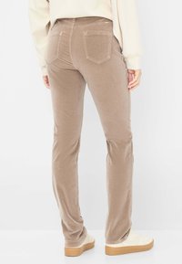 Beige fløjlsbukser med slim fit, der har to baglommer og en glat tekstur. Kombineret med cremede sneakers og en lys overdel.