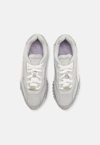 Harmaat urheilukengät, joissa on teksturoitu pinta, valkoiset kangasnauhat, pehmustettu nilkkapanta ja vastakkaisia korostuksia vaaleammassa harmaassa ja beigemäisessä sävyssä.