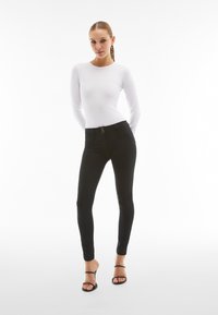 Top blanco de manga larga combinado con pantalones negros ajustados que cuentan con un cierre de doble botón y una tela lisa y elástica. Sandalias negras con tiras.