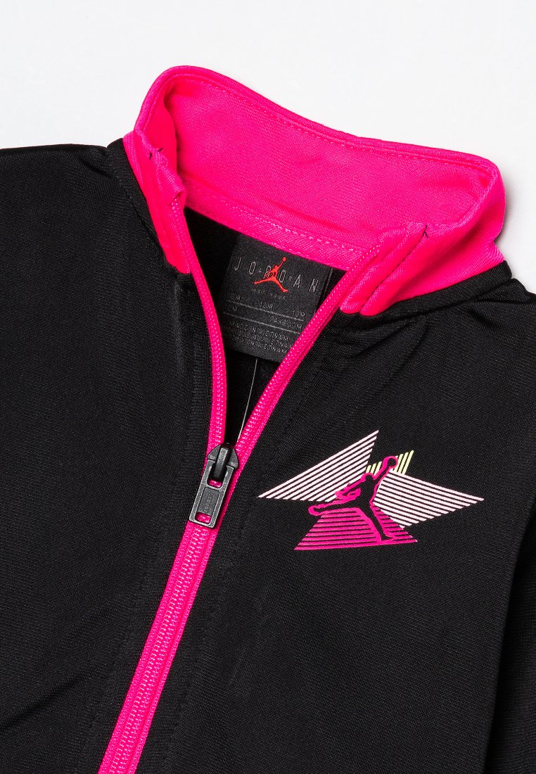 Veste de sport noire avec un col et une fermeture éclair roses. Présente un logo graphique Jordan en rose, jaune et blanc sur la poitrine. Texture douce.