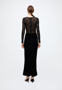 Black lace dress featuring long sleeves, fitted bodice, and a ruched velvet skirt with a side slit. The design is sleek and form-fitting.