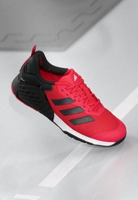 Red athletic shoe with black accents, textured mesh upper, three black stripes on the side, and a cushioned black heel section.