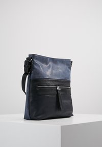 Leren schoudertas met een matte donkerblauwe bovenkant en een tekstuurlijke zwarte onderkant. Voorzien van een voorzak met rits en een verstelbare schouderband.