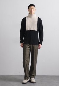 Cămășă neagră cu mânecă lungă, fular cu guler înalt cu nervuri fine, pantaloni olivi cu model și pantofi bej cu talpă închisă. Design simplu și modern.