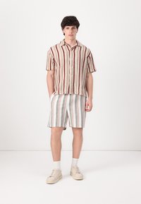 Cămașă cu mânecă scurtă, de culoare crem, cu dungi roșii și maronii; combinată cu pantaloni scurți raițați în culori pastel; teniși neutri și șosete albe.