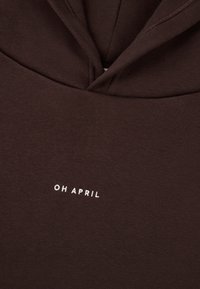 Barna kapucnis pulóver, puha anyagból készült, kenguru zsebbel és elöl fehér hímzett "OH APRIL" felirattal.