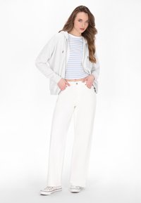 Grijze zip-up hoodie, blauw-witte gestreepte cropped shirt, witte wijde broek en witte sneakers met een lage profiel.