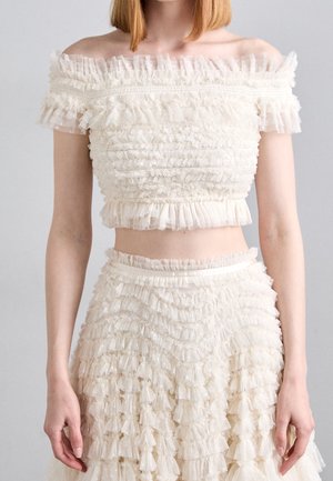Off-shoulder cream crop top and matching high-waist skirt featuring layered ruffled tulle fabric detailing.