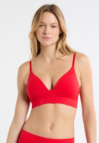 Czerwony trójkątny biustonosz typu bralette wykonany z miękkiej, fakturowanej tkaniny, wyposażony w cienkie, regulowane ramiączka oraz bezszwową konstrukcję, zapewniający gładki wygląd.