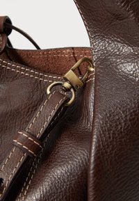 Sac à main en cuir marron avec une surface texturée, des coutures contrastantes, un clip en bronze robuste et une doublure intérieure douce.