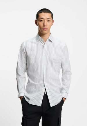 Witte overhemd met verticale blauwe strepen, voorzien van een puntige kraag en lange mouwen, gecombineerd met een zwarte broek.