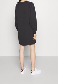 Svart sweatshirtklänning med vadderad struktur på axlarna, långa ärmar och en rundad fåll. Matchad med vita sneakers med brun detalj.