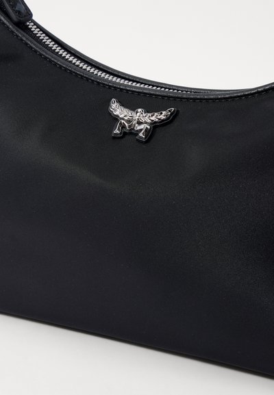 Melna auduma soma ar sudraba spārnu emblēmu un redzamu metāla rāvējslēdzēju gar augšējo malu.