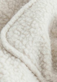 Tissu crème texturé avec une apparence douce et duveteuse, présentant un léger éclat et des bords surpiqués. Le matériau est épais et chaud.