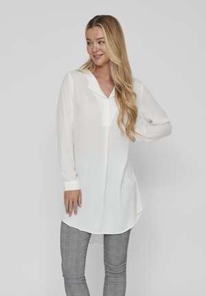 Balta, ilgomis rankovėmis palaidinė su apykakle, kišenės detalėmis ir išlenktomis kraštinėmis, pagaminta iš lengvos, permatomos medžiagos, derinama su languotais džinsais.