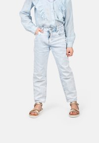 Jeans in denim azzurro chiaro con un design a gamba dritta, indossati con una blouse azzurro chiaro a rouches e sandali dorati, caratterizzati da un tessuto texture.