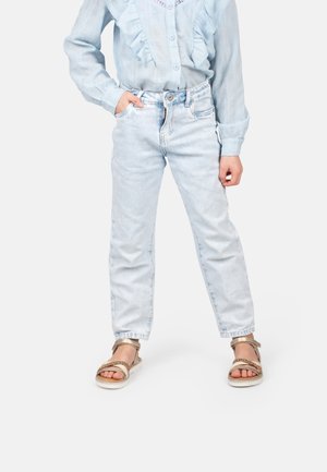 Helle blaue Jeans mit geradem Bein, kombiniert mit einer rüschierten hellblauen Bluse und goldenen Sandalen, aus einem strukturierten Stoff.