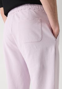 Lyslilla sweatpants med elastisk talje, baglomme detaljer og glat bomuldsstruktur. Vinklet udsigt fra bagfra, der viser pasformen.