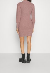 Robe en maille côtelée et ajustée couleur rose poudré, dotée de manches longues bouffantes et d'un col montant, associée à des bottines noires à semelle épaisse.