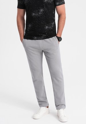 Pantalons de survêtement en coton gris à coupe décontractée, avec poches latérales et texture lisse. Assortis à un t-shirt noir à motifs et des baskets blanches.